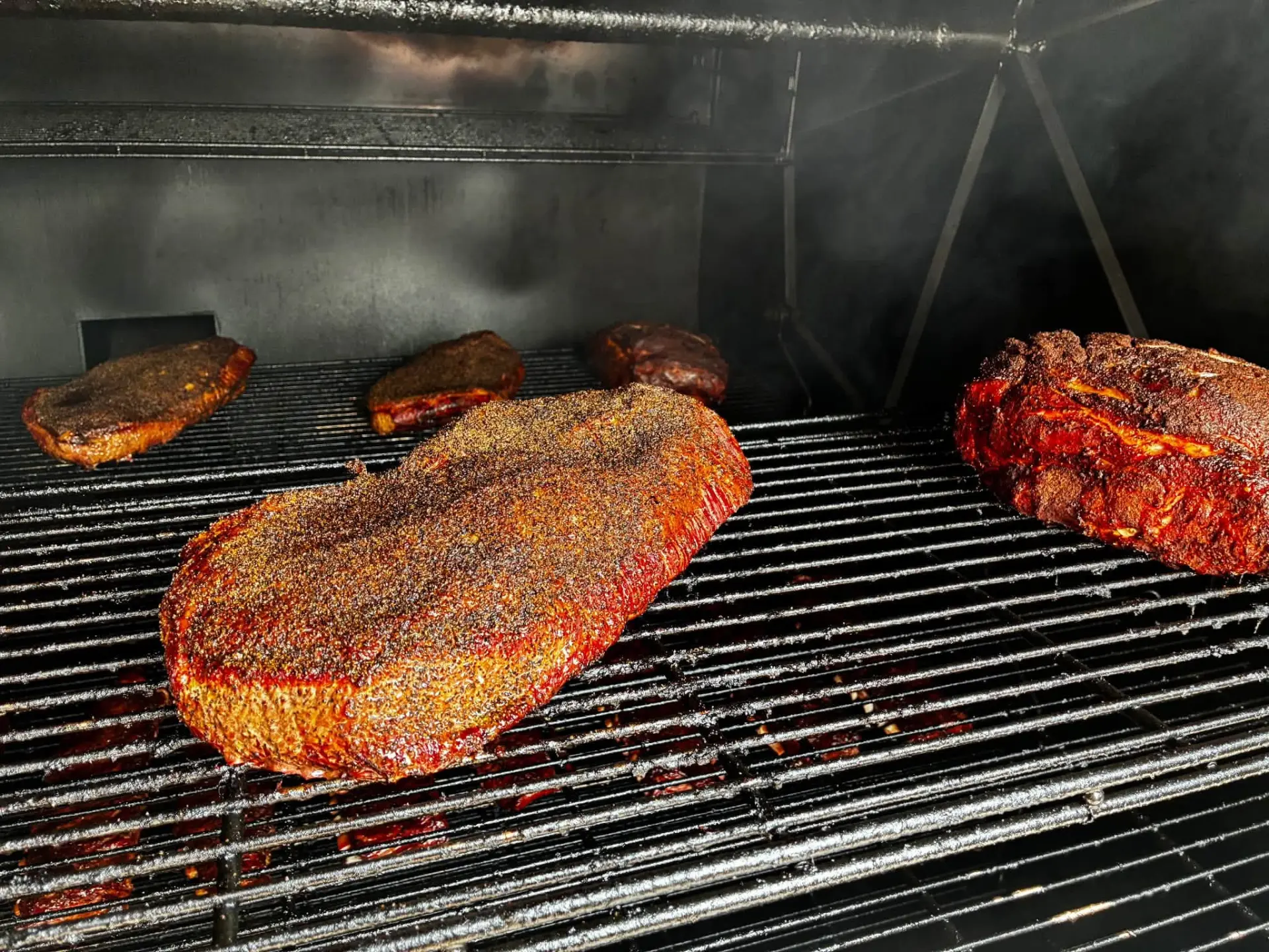 Hardwood-smoked brisket at PIT14 Barbecue in Spearfish, SD Brisket smoking on the grates of a traditional offset smoker at PIT14
